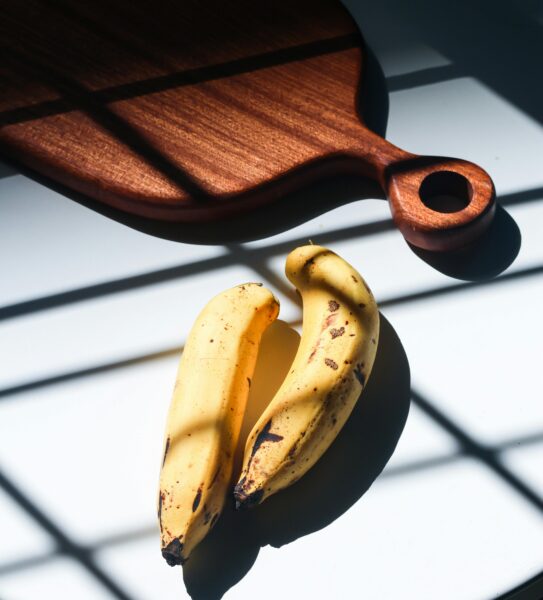 Creative arrangement of ripe bananas on a sunlit surface with a wooden cutting board casting shadows.