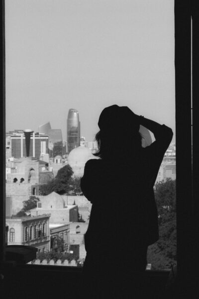 Silhouette of a woman gazing out at a city skyline through a window.