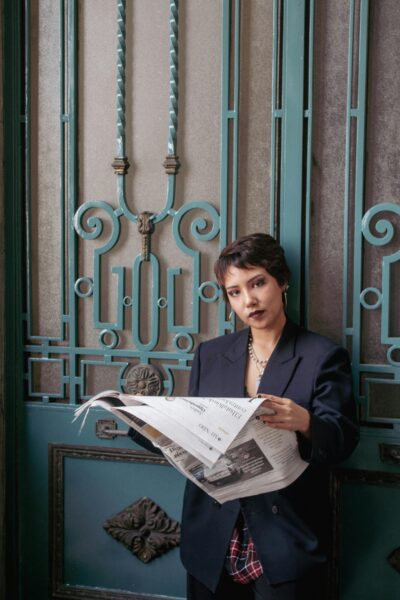 A fashionable woman in a blazer reads a newspaper against an elegant door backdrop