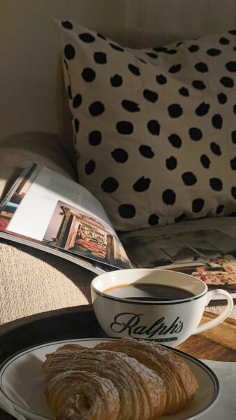 A relaxing morning setup with coffee, croissant, and a magazine on a couch.