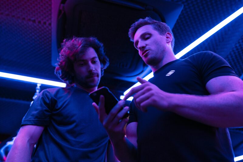Two men engaging in a focused discussion while looking at a smartphone in a gym setting.