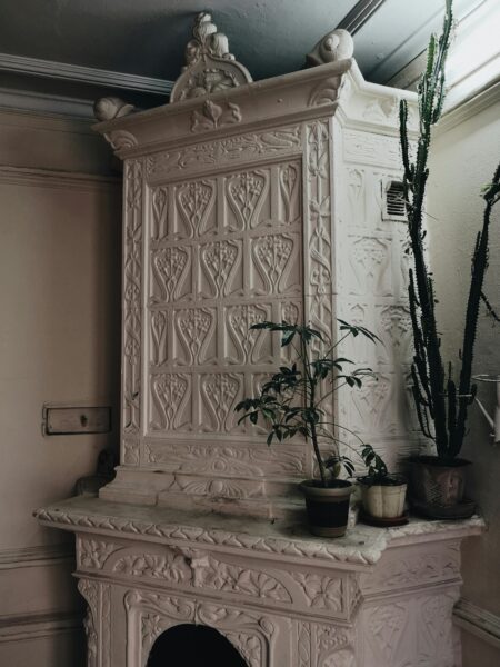 Green potted plants placed on vintage white stucco fireplace with ornamental carving in room