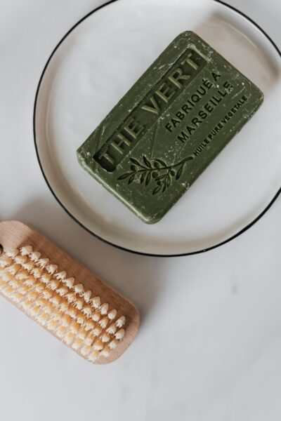 Minimalist composition of a green soap and wooden brush on a white plate.