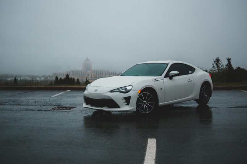 Contemporary white automobile on shabby roadway behind old building under foggy sky in daylight