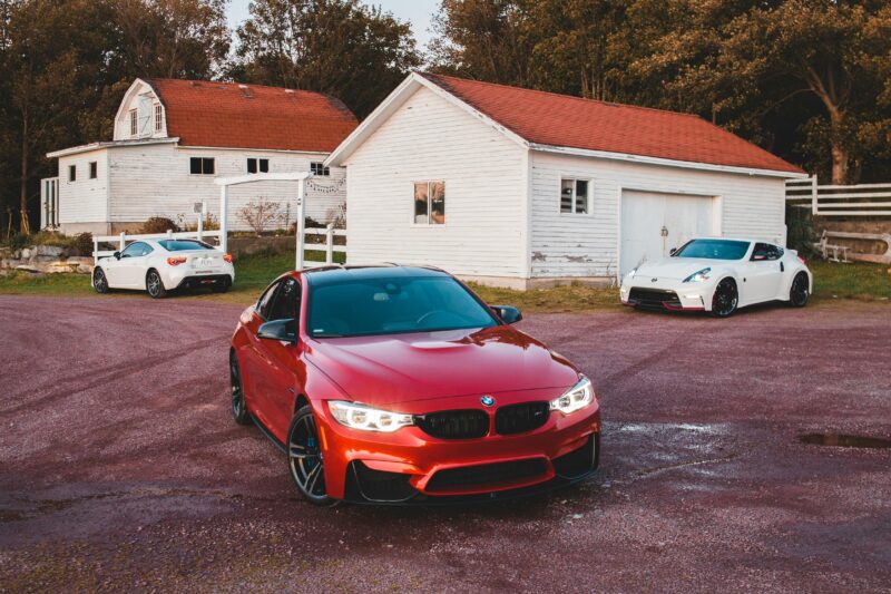 Three luxury cars parked peacefully in a scenic rural setting with quaint houses.