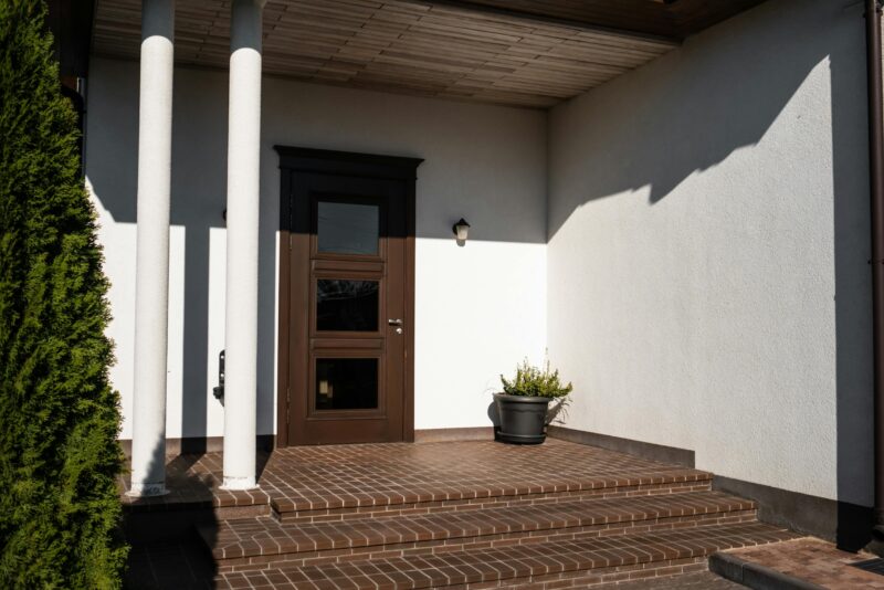 Contemporary house entrance featuring brown door, brick steps, and decorative columns.