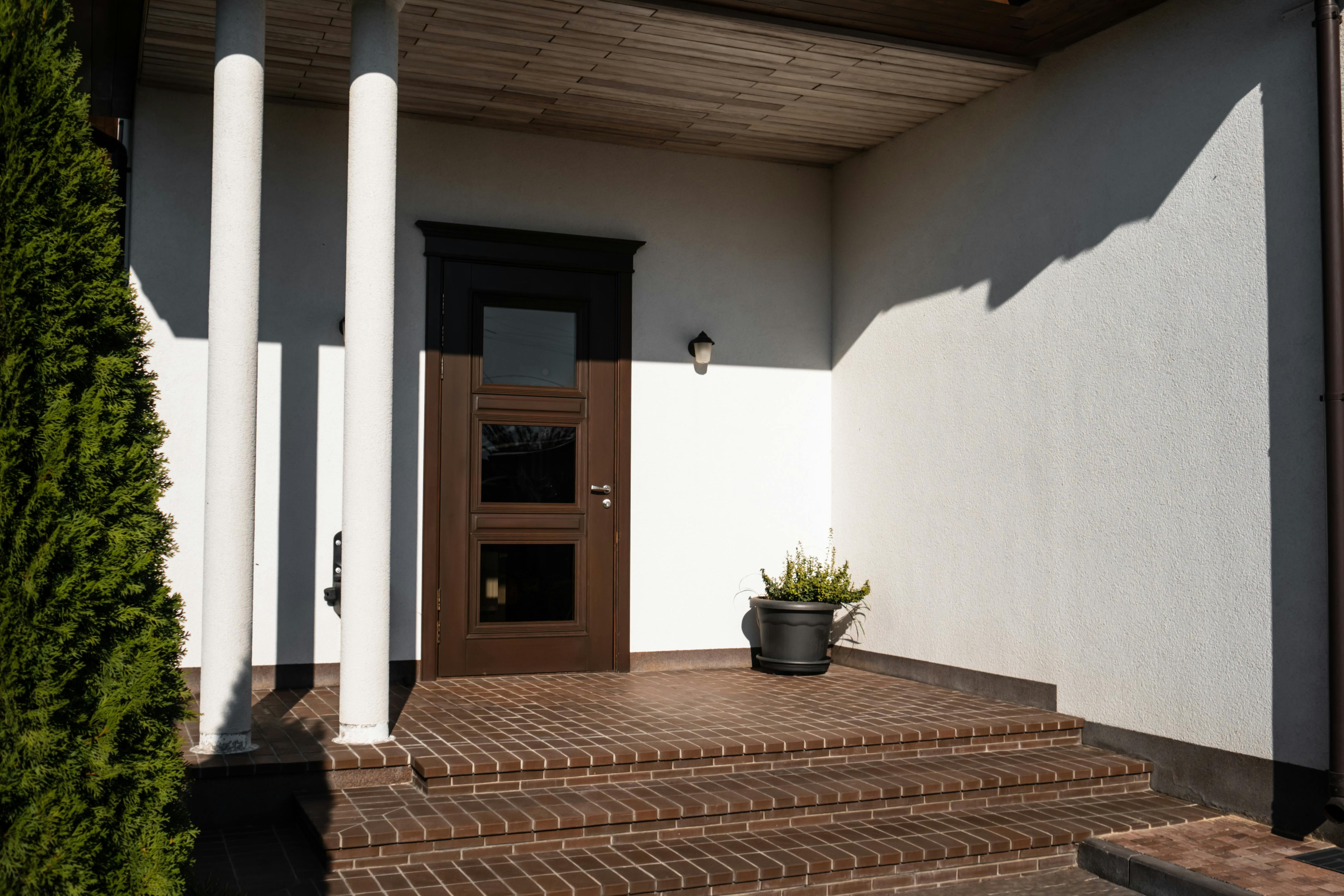 Contemporary house entrance featuring brown door, brick steps, and decorative columns.