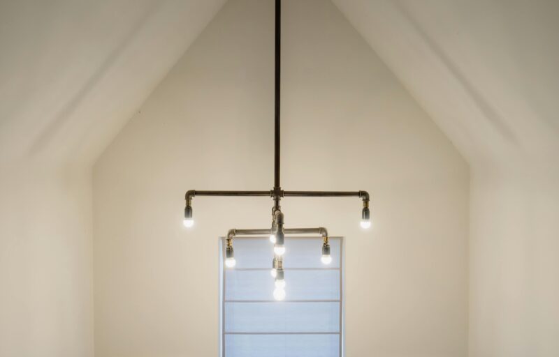 A minimalist interior featuring an industrial-style pipe light fixture hanging from a vaulted ceiling.