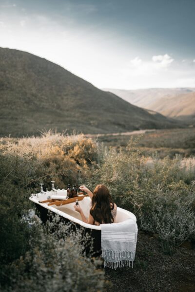 A woman relaxes in an outdoor bathtub surrounded by nature, capturing tranquility.