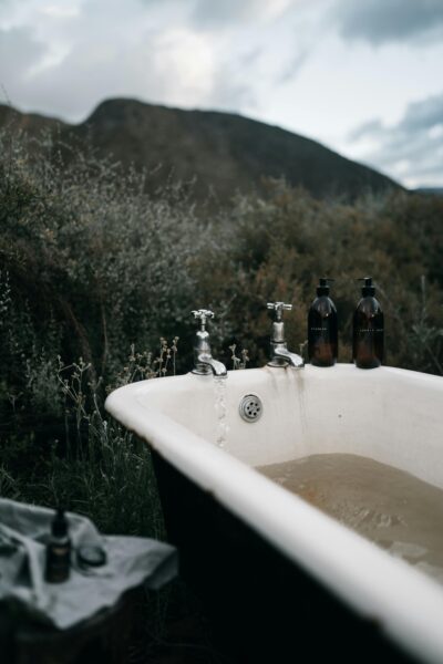 Outdoor vintage bathtub with running water and bath essentials in a natural setting.