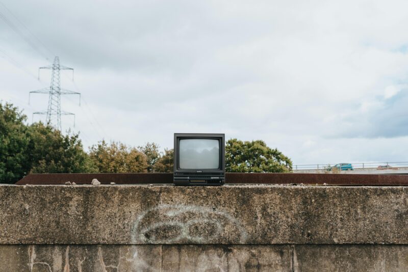 Retro TV set sits on a graffitied concrete wall with trees and power lines in the background.