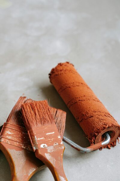 A detailed view of paintbrushes and a roller with brown paint on a gray surface.