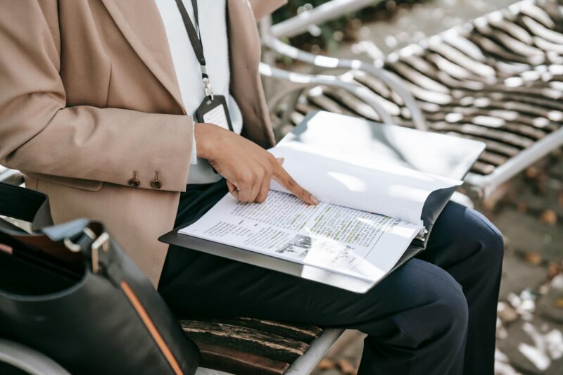 A woman reviewing documents on a park bench during daytime, focusing on work or study.