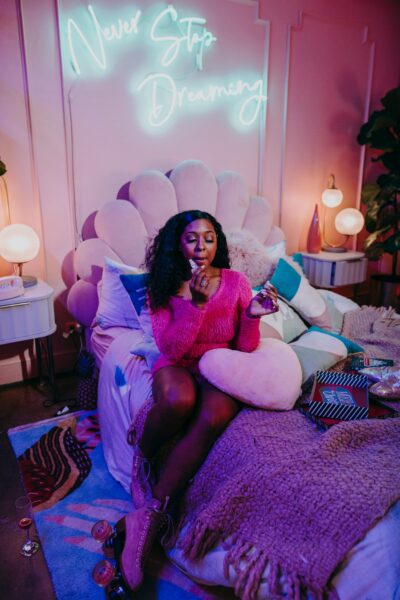 Teen girl in a cozy, stylish bedroom with neon 'Never Stop Dreaming' sign.