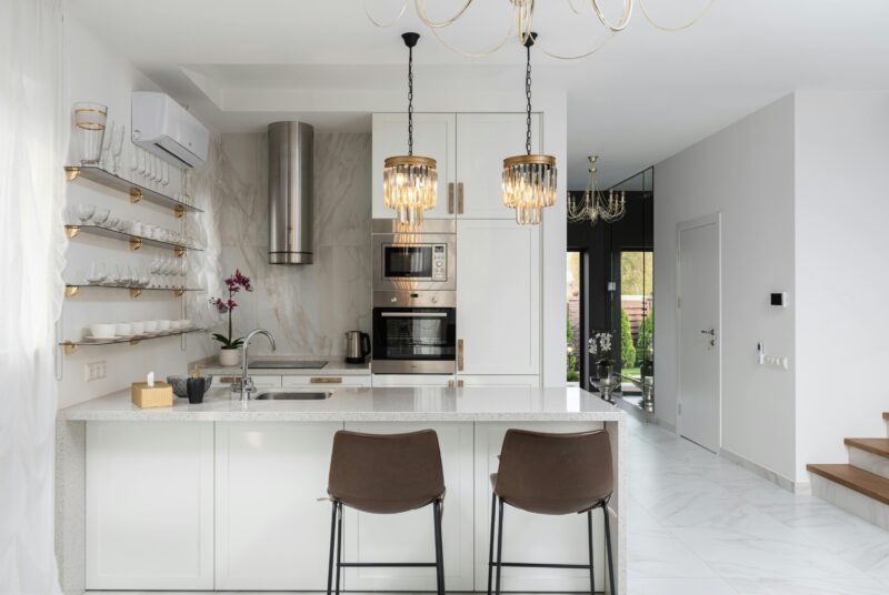 Interior of contemporary kitchen with modern appliances and chairs at white counter.