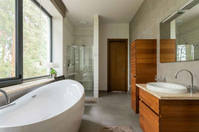 Spacious bathroom featuring a sleek bathtub, wooden vanity, and large window.