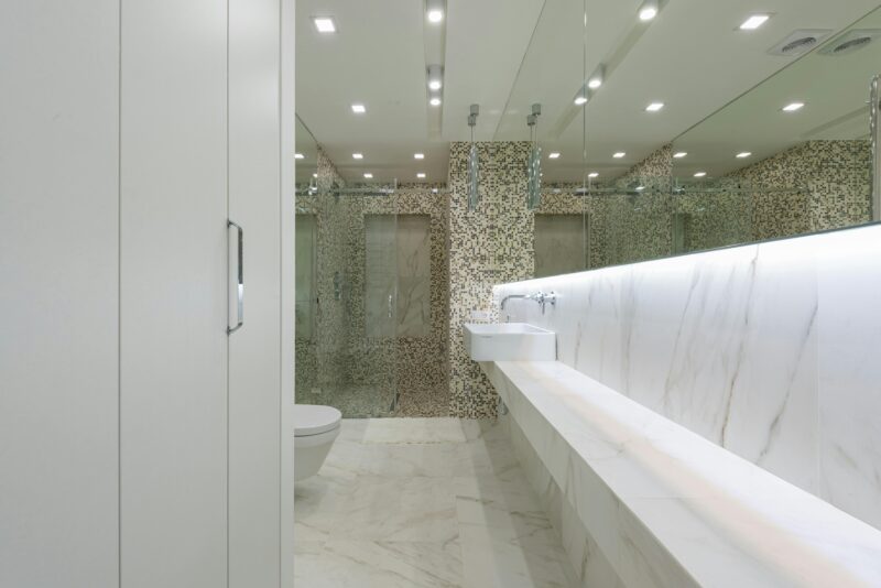 Contemporary restroom with marble tile and toilet behind glass wall with sink under mirror