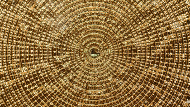 A detailed image of a golden circular metal texture with intricate geometric patterns.