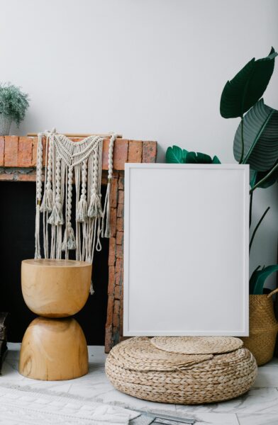 Composition of empty white photo frame placed near brick fireplace and cozy decorations in light room.