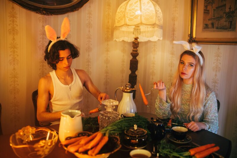 Two teenagers in bunny ears enjoying an Easter-themed dinner indoors with carrots and vintage decor.