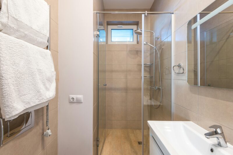 Contemporary bathroom featuring a glass shower, beige tiles, and a sleek sink area.