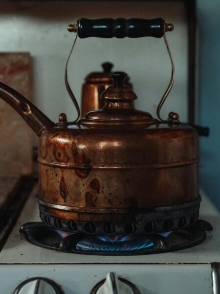 A nostalgic scene of a vintage copper kettle heating on a gas stove, showcasing rustic charm.