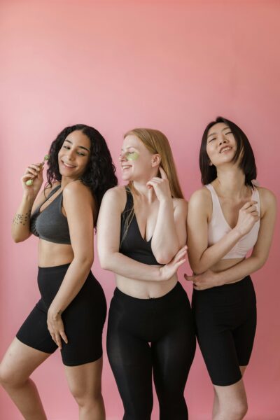 Three women wearing activewear having fun indoors with a pink background.