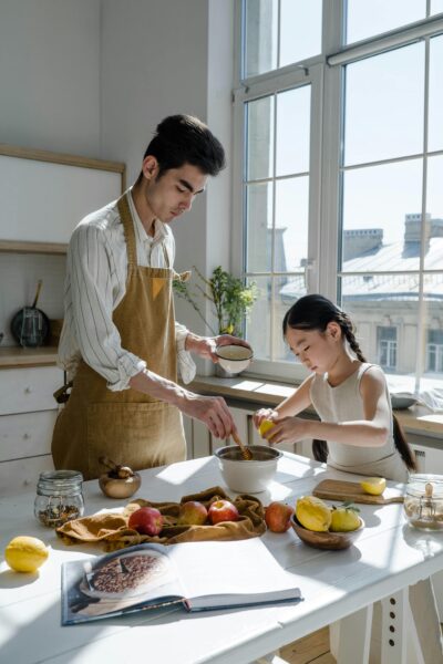 Father and daughter enjoying baking in a bright kitchen, surrounded by fruit and fresh ingredients.