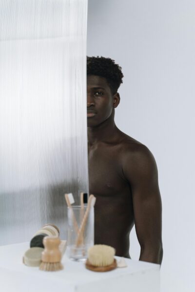 Artistic image of a shirtless man behind glass, with grooming items in a minimalist setting.