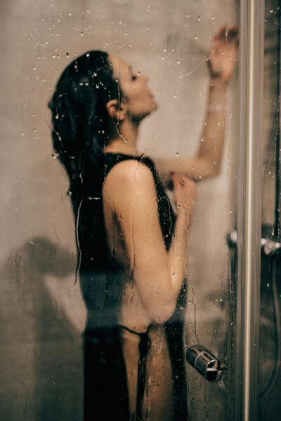 Moody portrait of a woman standing behind a wet glass door with water droplets.