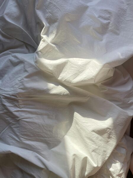 A close-up of smooth white linen with natural creases under soft daylight, creating a tranquil and minimalist composition.