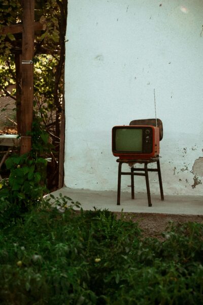 A classic vintage television set outdoors leaning against a rustic wall surrounded by greenery.
