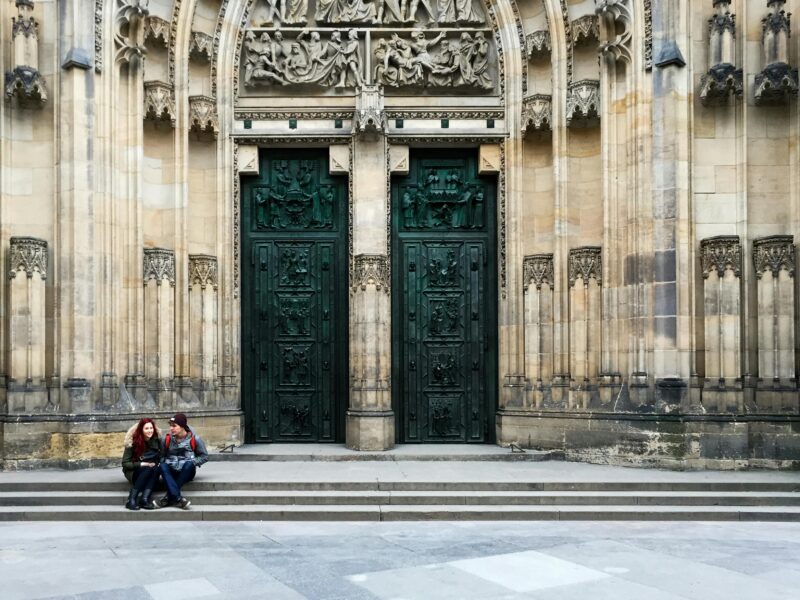 A couple relaxes on steps outside the grand doors of St. Vitus Cathedral in Prague.