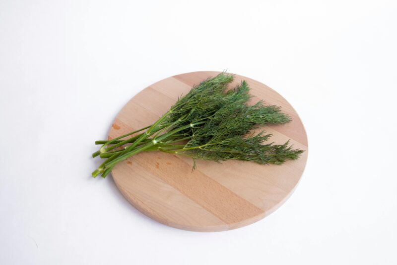 High-quality image of fresh dill sprigs on a wooden cutting board against a white background.