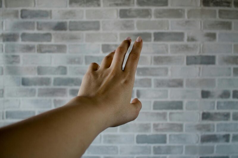 A hand reaching towards a whitewashed brick wall indoors, showcasing texture and depth.