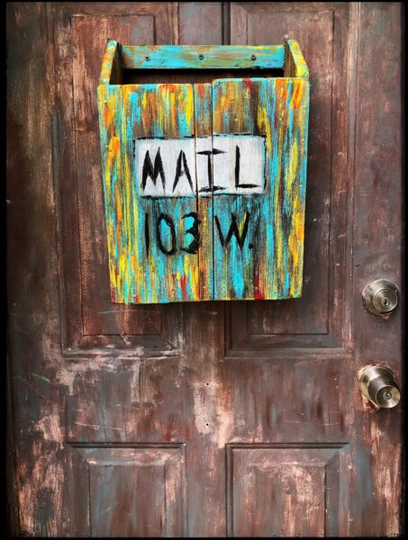 Colorful rustic mailbox labeled 'MAIL 103 W' on a distressed wooden door in Hidalgo, TX.