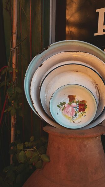 Stack of vintage enamel bowls with floral decor in a rustic setting.
