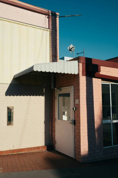 Pink and brown concrete building with white awning under blue sky.