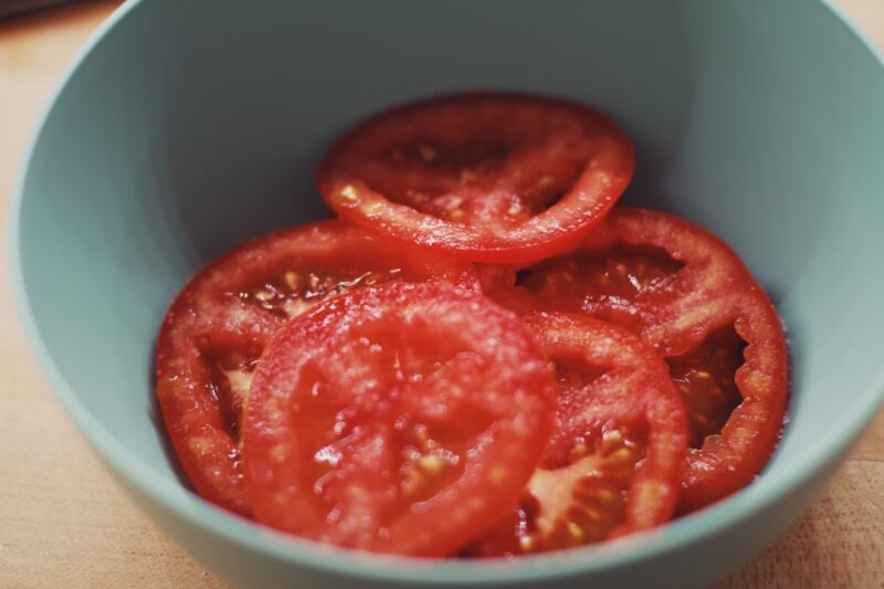 Sliced tomatoes in a teal bowl on a cutting board.