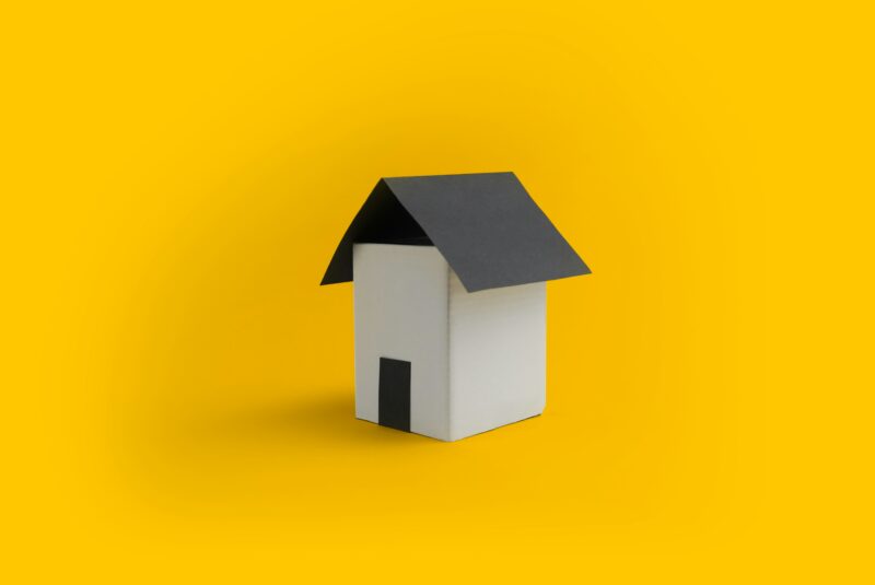 A white house with a black roof on a yellow background.