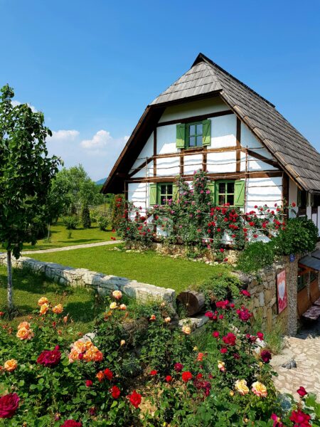 Brown wooden house surrounded by green trees and flowers under blue sky during daytime