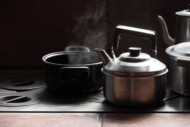 Stainless steel kettle beside black ceramic mug on white table.