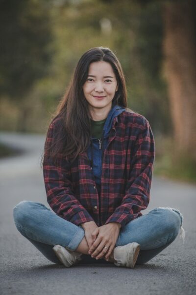 Woman in red and black plaid dress shirt and blue denim jeans sitting on gray rock
