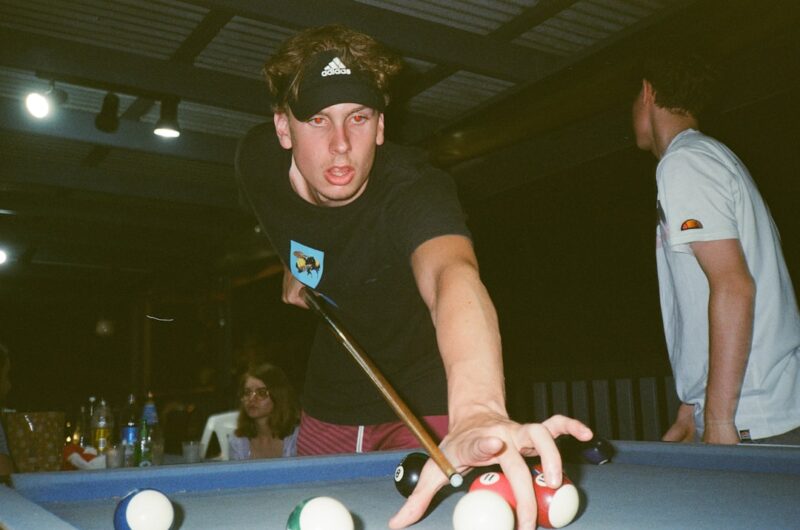 Man in black crew neck t-shirt and black fitted cap playing billiard.