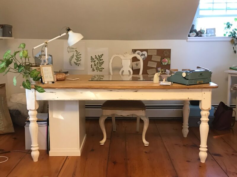 A room with a desk, chair, lamp and pictures on the wall
