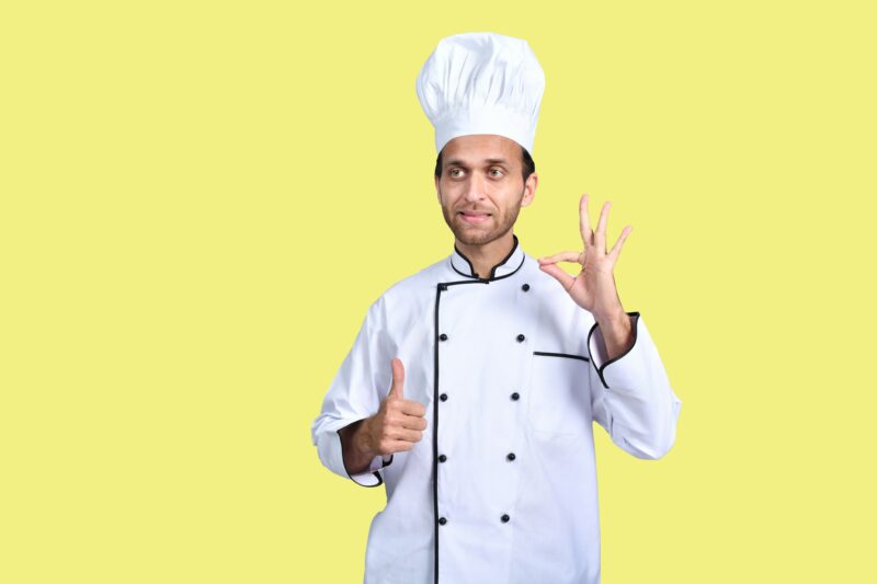 A man wearing a chef's hat and holding his hands up