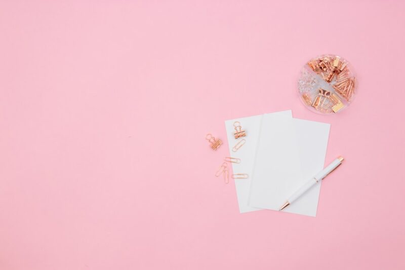 Blush office supplies with a notepad, pen, and a pair of scissors.