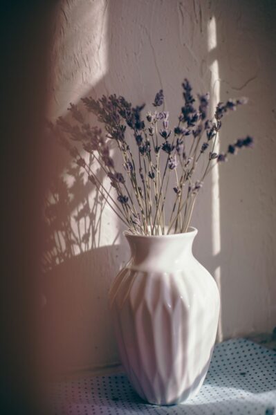 A white vase filled with lots of purple flowers.