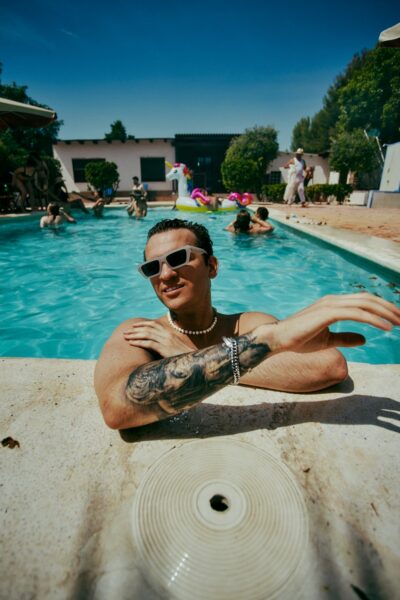 A man with tattoos sitting in front of a swimming pool.