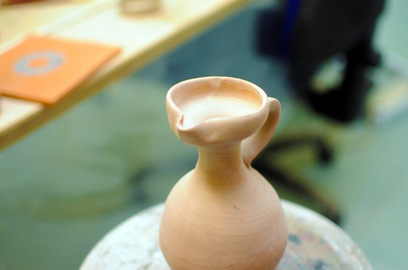 Handcrafted ceramic vase sitting on a table next to a mirror.
